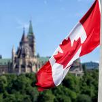 Un drapeau canadien flotte au vent, avec le Parlement en arrière-plan.