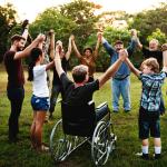 Person in a wheelchair holding hands with people standing in a circle in a park
